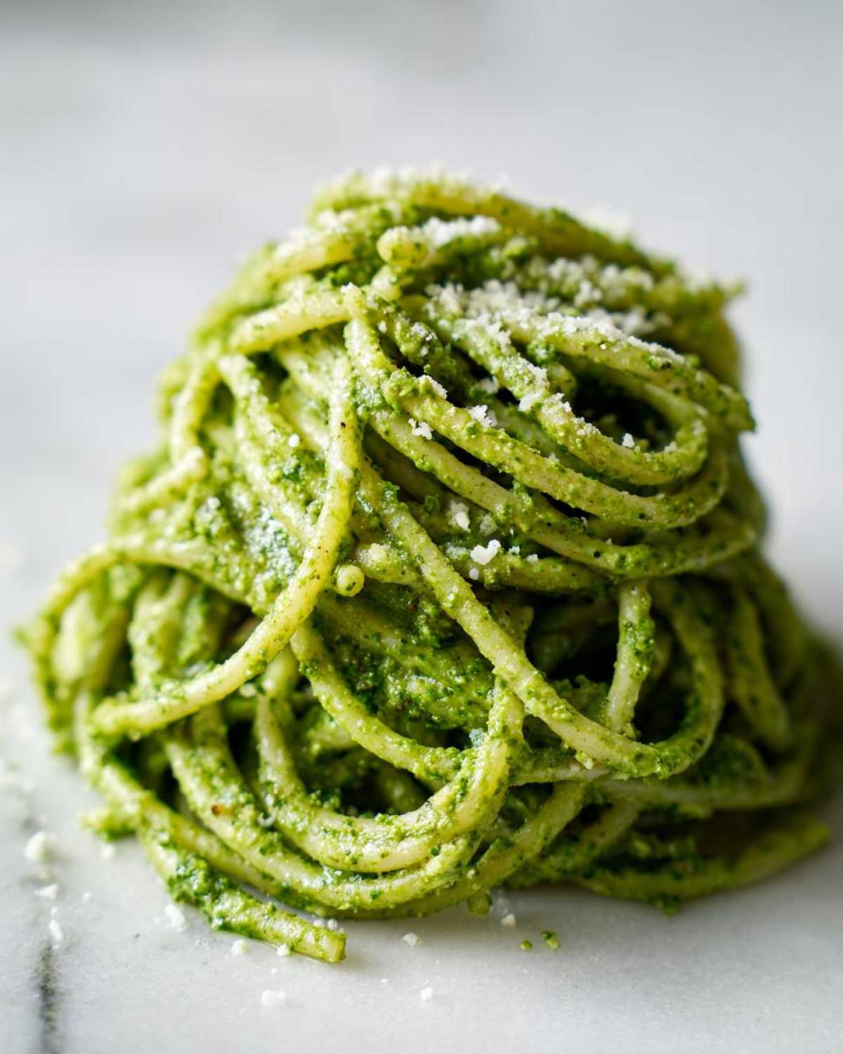 A tall swirl of protein pasta tossed in bright green pesto sauce and topped with grated cheese.