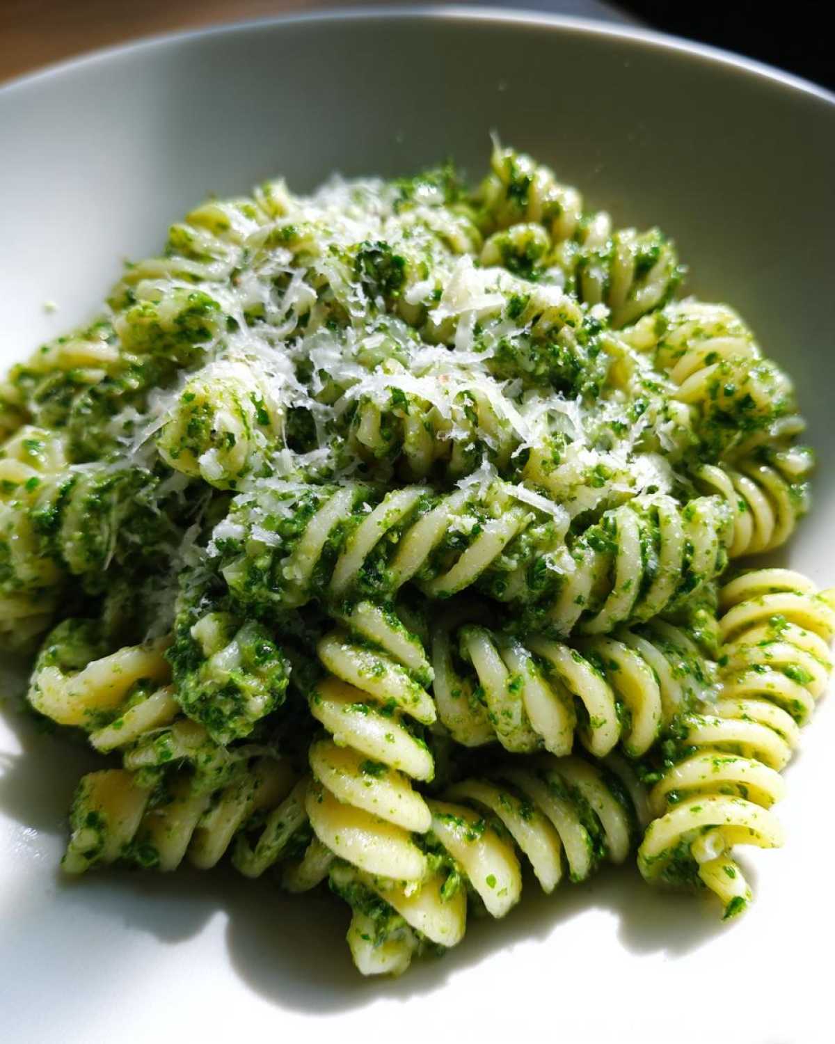 Close-up of fusilli protein pasta tossed in green pesto sauce and topped with grated cheese.