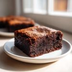 A close-up of a fudgy square of homemade 4 ingredient cottage cheese brownies resting on a small white plate.