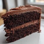 Close-up of a rich, dark slice of homemade chocolate cake layered with smooth chocolate frosting.