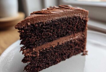 Close-up of a rich, dark slice of homemade chocolate cake layered with smooth chocolate frosting.