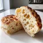Close-up of homemade english muffins cut in half, revealing a light, airy interior texture full of characteristic nooks and crannies.