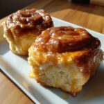 Two freshly baked, sticky glazed honey buns served on a white rectangular plate, showcasing the soft interior.