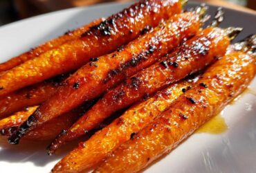 Close-up of several perfectly cooked honey glazed carrots with a shiny, caramelized coating resting on a white plate.