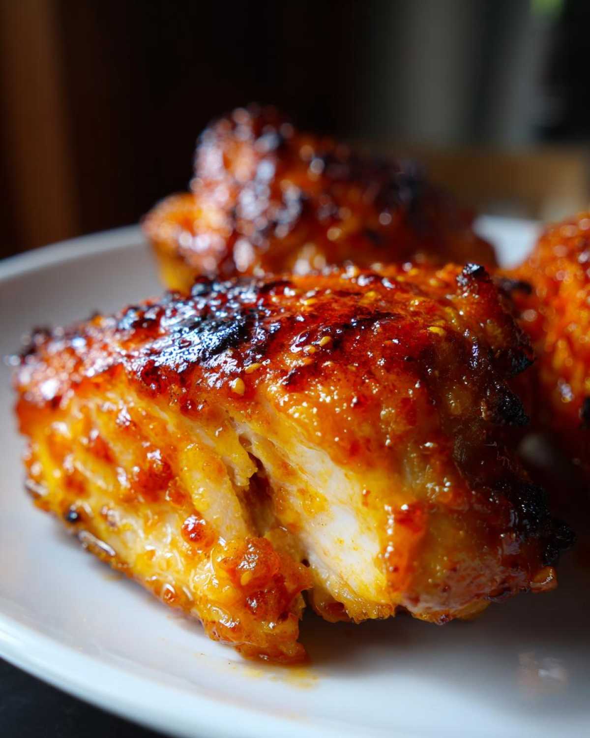 Close-up of a piece of hot honey chicken cut open, showing juicy white meat coated in a sticky, spicy-sweet glaze.