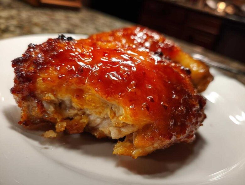 A close-up of a piece of hot honey chicken with a thick, shiny, reddish-orange glaze on a white plate.