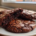 Close-up of fudgy brownie cookies, one broken in half to show the rich interior texture.