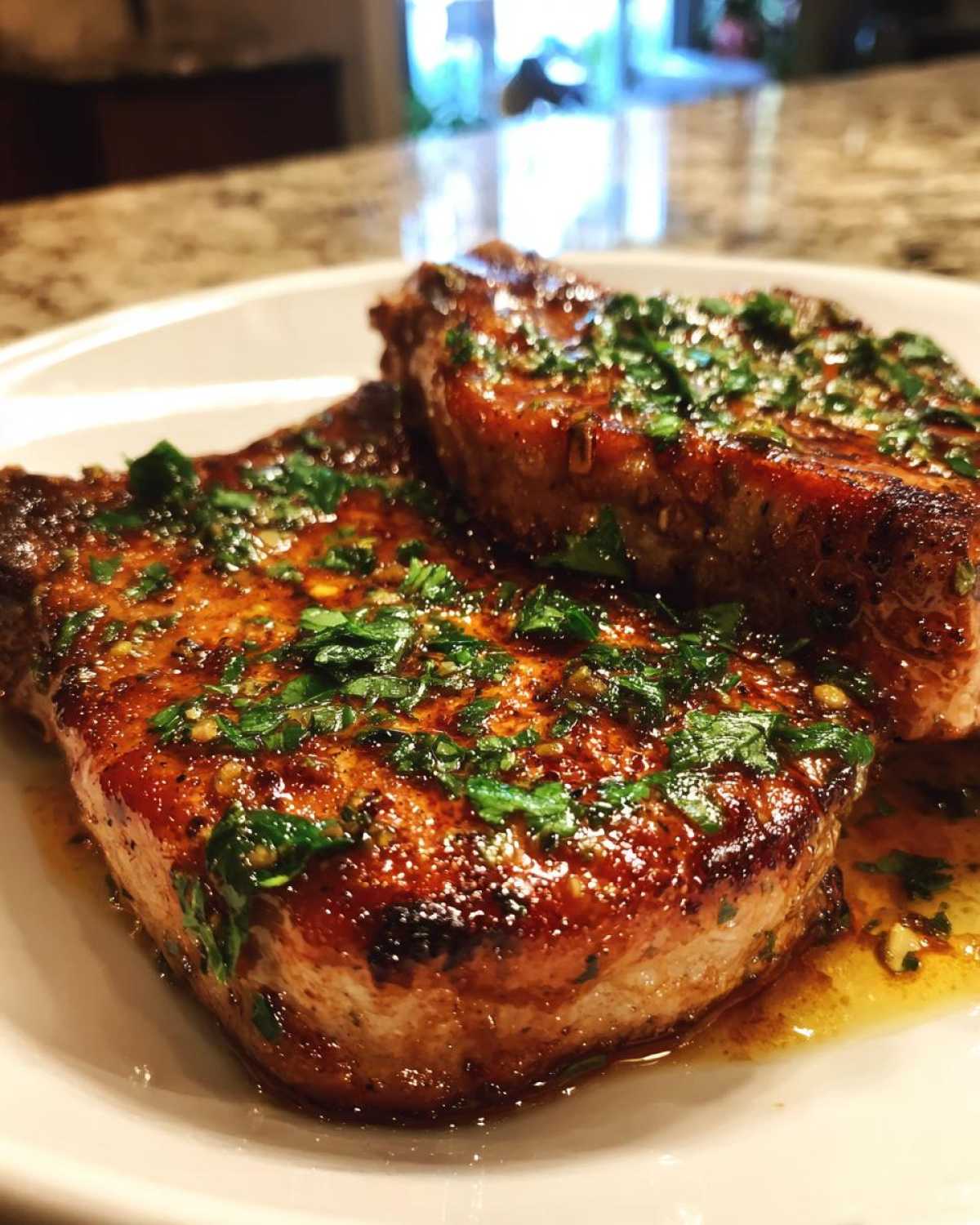 Close-up of two perfectly seared and glazed pork chops topped with fresh chopped parsley.
