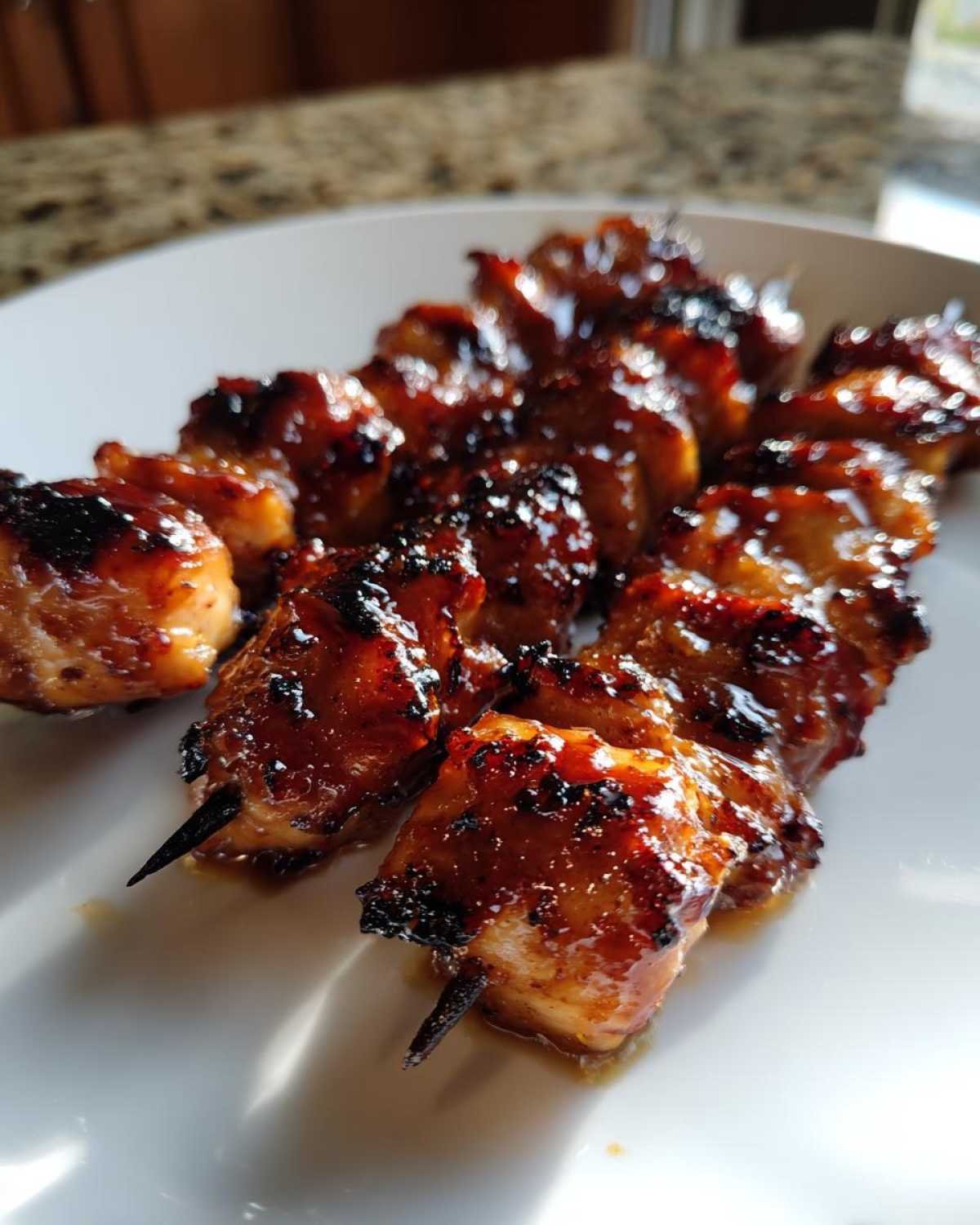Close-up of juicy, glazed honey garlic chicken skewers resting on a white plate, showing caramelized edges.