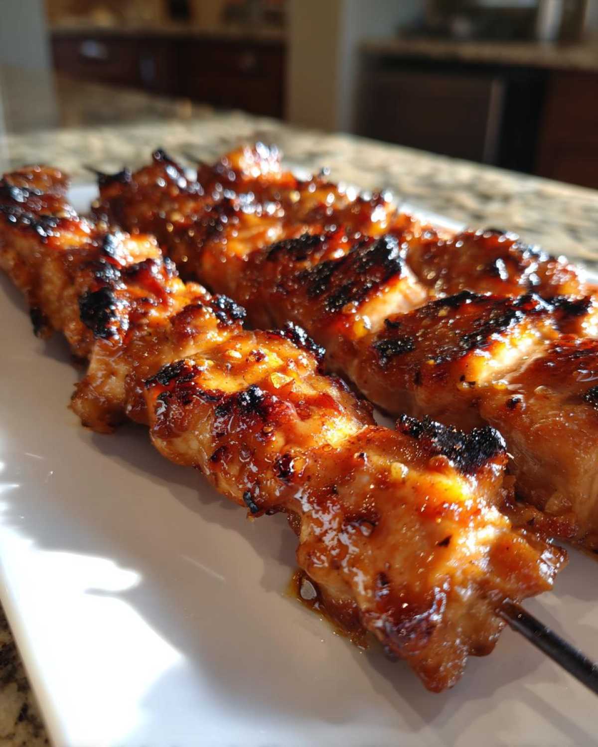Close-up of several glossy, caramelized honey garlic chicken skewers resting on a white platter.