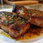 Two thick, juicy pork chops seared to perfection and covered in a glossy garlic butter sauce and fresh parsley.