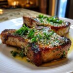 Two thick, juicy pork chops seared golden brown and topped with a glistening garlic herb butter sauce.