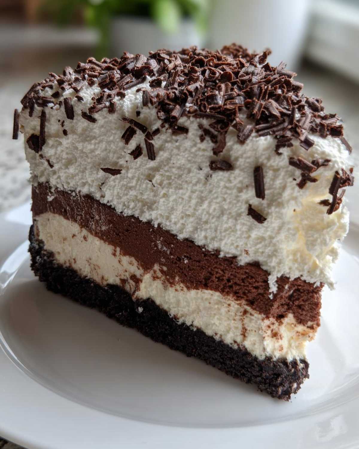 A decadent slice of layered mud pie featuring a dark crust, alternating chocolate and vanilla mousse layers, topped with whipped cream and chocolate shavings.