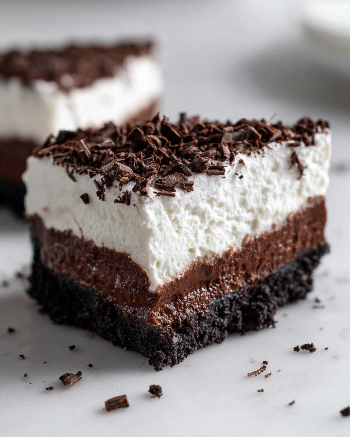 Close-up of a decadent slice of mud pie showing a dark cookie crust, chocolate layer, white cream layer, and chocolate shavings.