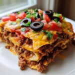 A generous slice of 8-layer mexican pizza, showing layers of seasoned beef and cheese, topped with tomatoes, olives, and cilantro.