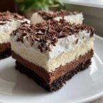 A close-up of a rich, layered slice of mud pie featuring a dark crust, chocolate mousse, vanilla layer, and whipped cream topped with chocolate shavings.