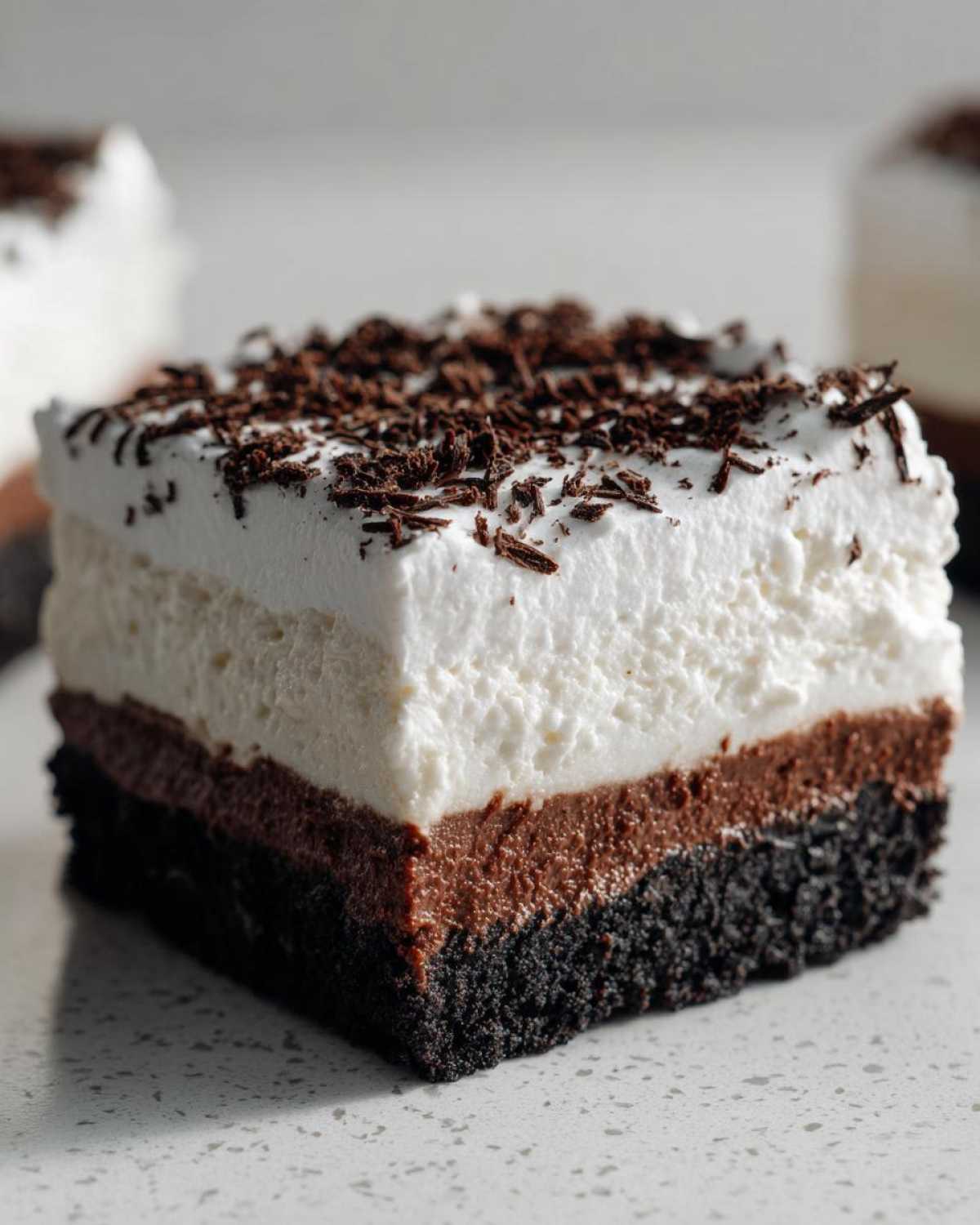 Close-up of a decadent slice of mud pie showing dark crust, chocolate layer, white cream layer, and chocolate shavings.