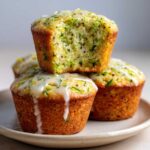 A stack of three Lemon Poppy Seed Zucchini Muffins, one on top is broken open showing the moist interior.