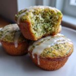 Close-up of three Lemon Poppy Seed Zucchini Muffins stacked, one cut open showing moist texture and zucchini shreds.