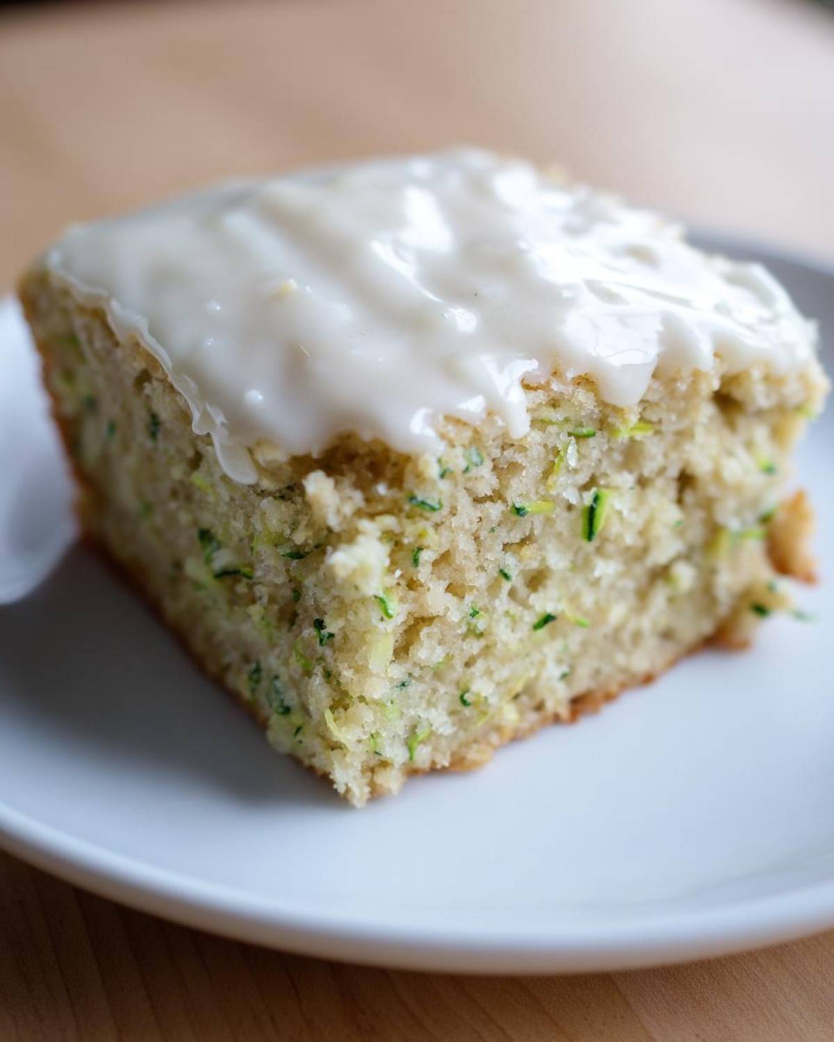Close-up of a single serving of Lemon Zucchini Bars with Glaze on a white plate.
