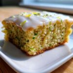 Close-up of a single square of Lemon Zucchini Bars with Glaze, showing the moist crumb and white icing topped with zest.
