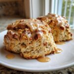 Two freshly baked Maple Pecan Scones generously topped with a thick, dripping maple glaze on a white plate.