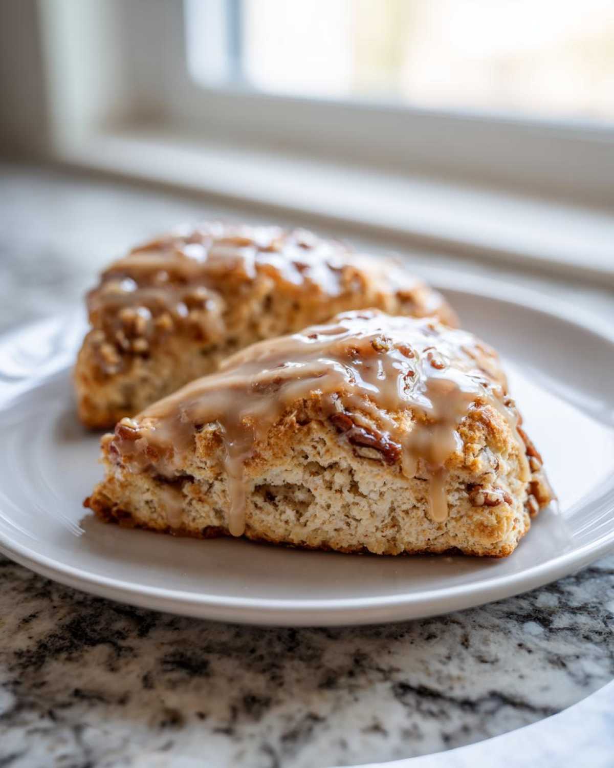 Two freshly baked Maple Pecan Scones topped with a thick, dripping maple glaze on a white plate.