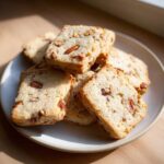 A stack of golden Maple Pecan Shortbread Cookies with visible pecan pieces on a light ceramic plate.