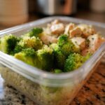 A clear plastic meal prep container filled with healthy food: chicken pieces, bright green broccoli, and quinoa. This shows how to eat healthy wrong for busy.