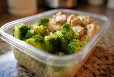 A clear plastic meal prep container filled with healthy food: chicken pieces, bright green broccoli, and quinoa. This shows how to eat healthy wrong for busy.