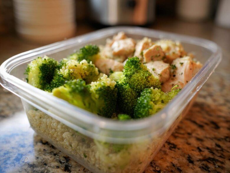 A clear plastic meal prep container filled with healthy food: chicken pieces, bright green broccoli, and quinoa. This shows how to eat healthy wrong for busy.