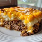 A hearty slice of meatloaf casserole featuring a ground meat base topped with mashed potatoes and melted cheddar cheese.