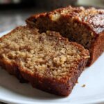 Close-up of two moist slices cut from a loaf of golden brown banana bread recipe, showing a rich, speckled crumb.