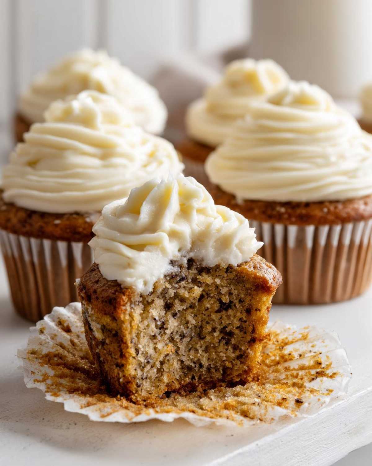 Close-up of a moist banana cupcakes with a bite taken out, revealing the speckled interior and topped with rich cream cheese frosting.