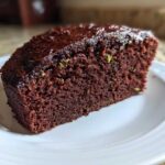 A close-up of a slice of Top Rated Moist Chocolate Zucchini Cake with dark chocolate glaze.