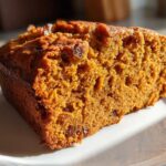 Close-up of a moist slice of easy pumpkin bread with visible raisins, sitting on a white plate.