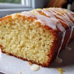 Close-up of a slice of incredibly moist olive oil cake loaf topped with a white lemon glaze and zest.