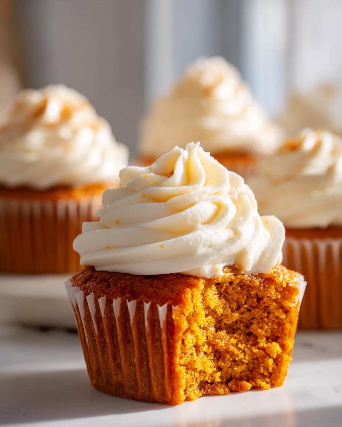Close-up of a moist pumpkin spice cupcakes with a bite taken out, topped with swirled cream cheese frosting.
