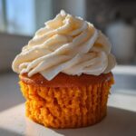 Close-up of a single, moist pumpkin spice cupcake topped with a swirl of white cream cheese frosting.