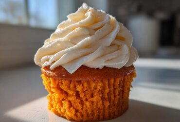 Close-up of a single, moist pumpkin spice cupcake topped with a swirl of white cream cheese frosting.