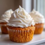 Close-up of a moist pumpkin spice cupcake topped with a swirl of white cream cheese frosting.