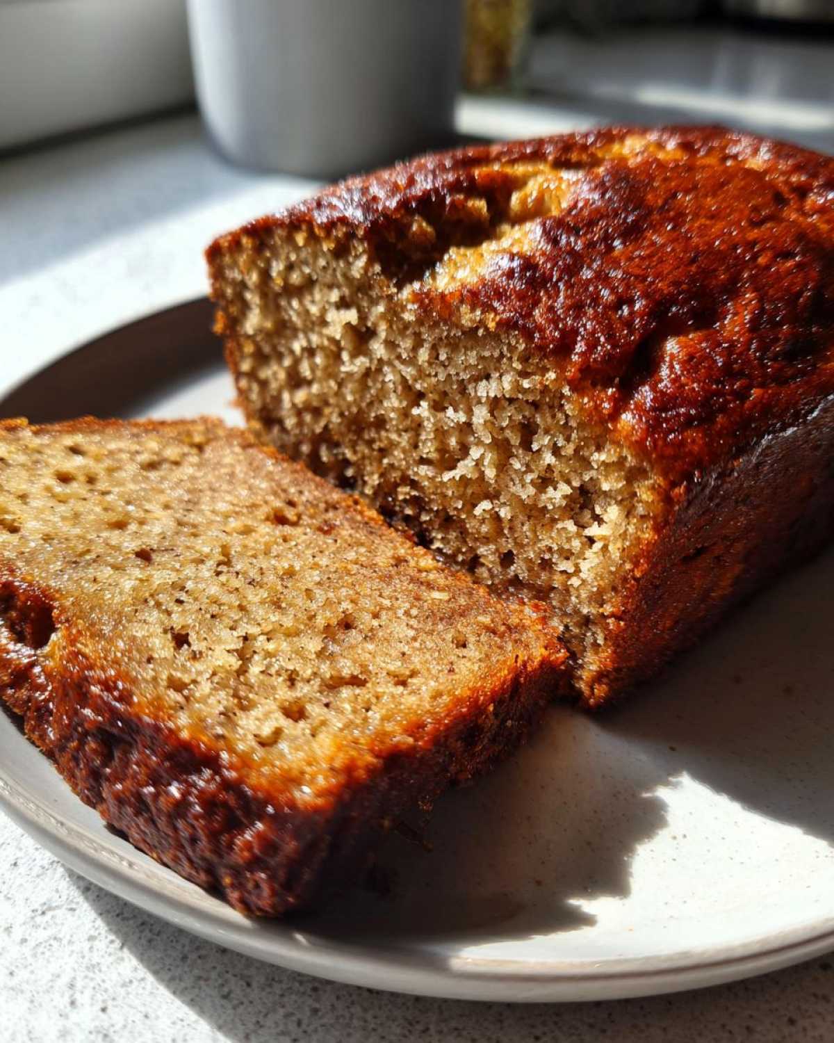 Close-up of a moist slice cut from a loaf of banana bread recipe, showing a rich, golden-brown crust.