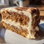 Close-up of a moist slice of spice cake layered with cream cheese frosting and dusted with cinnamon.