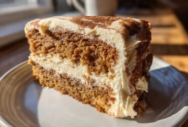 Close-up of a moist slice of spice cake layered with cream cheese frosting and dusted with cinnamon.