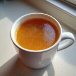 Close-up of a white mug filled with warm, golden-orange bone broth recipe liquid, sitting on a light countertop.