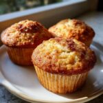 Three freshly baked one bowl apple muffins with golden brown, slightly crumbly tops sitting on a white plate.