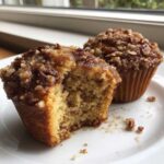 Close-up of two pecan pie muffins, one bitten into, showing the moist interior and pecan streusel topping.