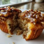 A pecan pie muffin cut in half, revealing a moist, cakey interior and a sticky, glazed pecan topping.