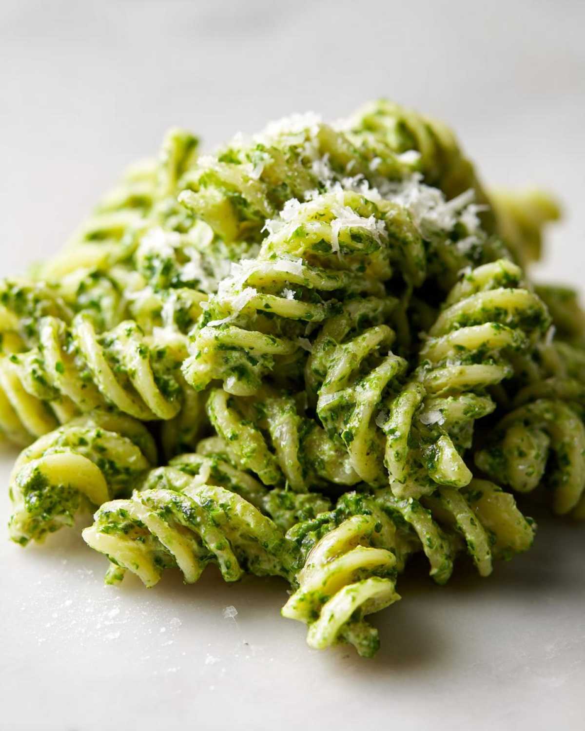 Close-up of rotini protein pasta tossed in vibrant green pesto sauce and topped with grated parmesan.