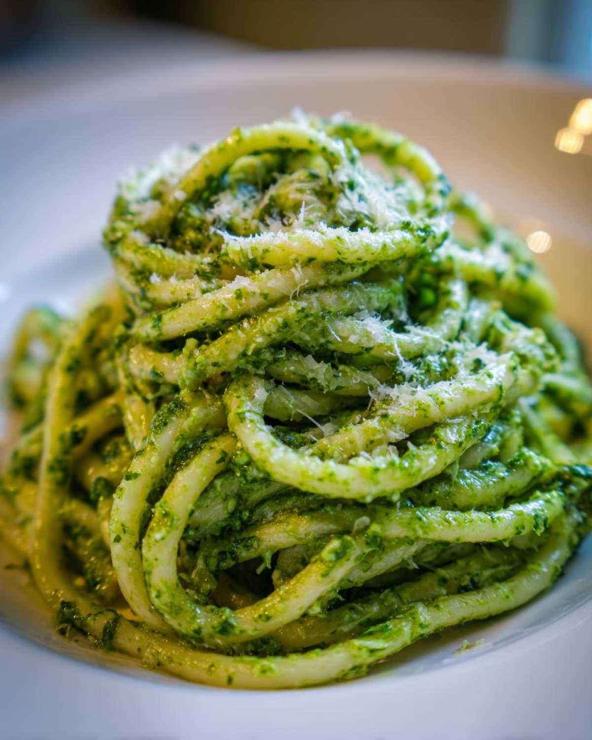 Close-up of thick, coiled protein pasta coated in vibrant green pesto sauce and topped with grated cheese.
